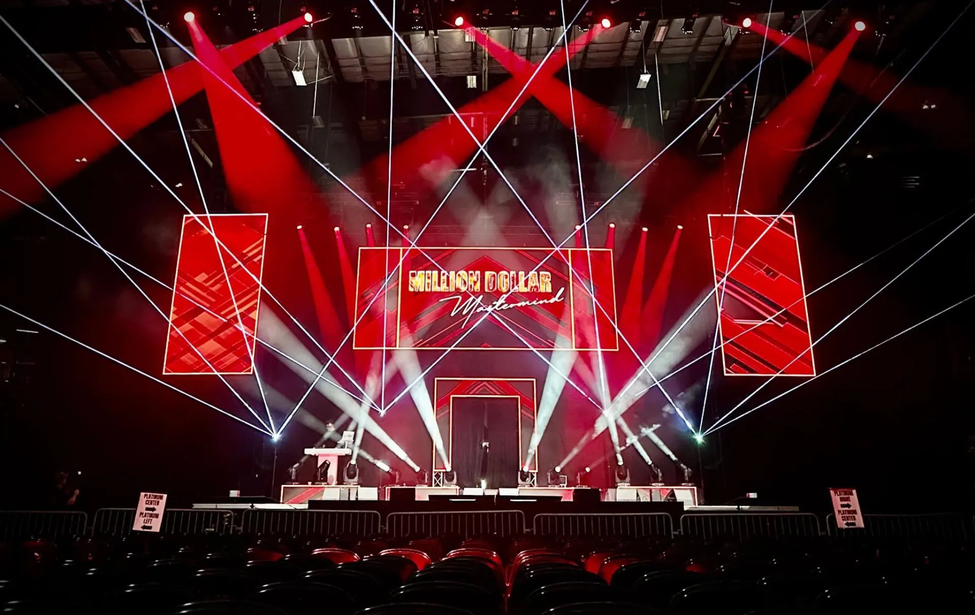 A dramatic live production stage bathed in red laser beams and geometric light panels